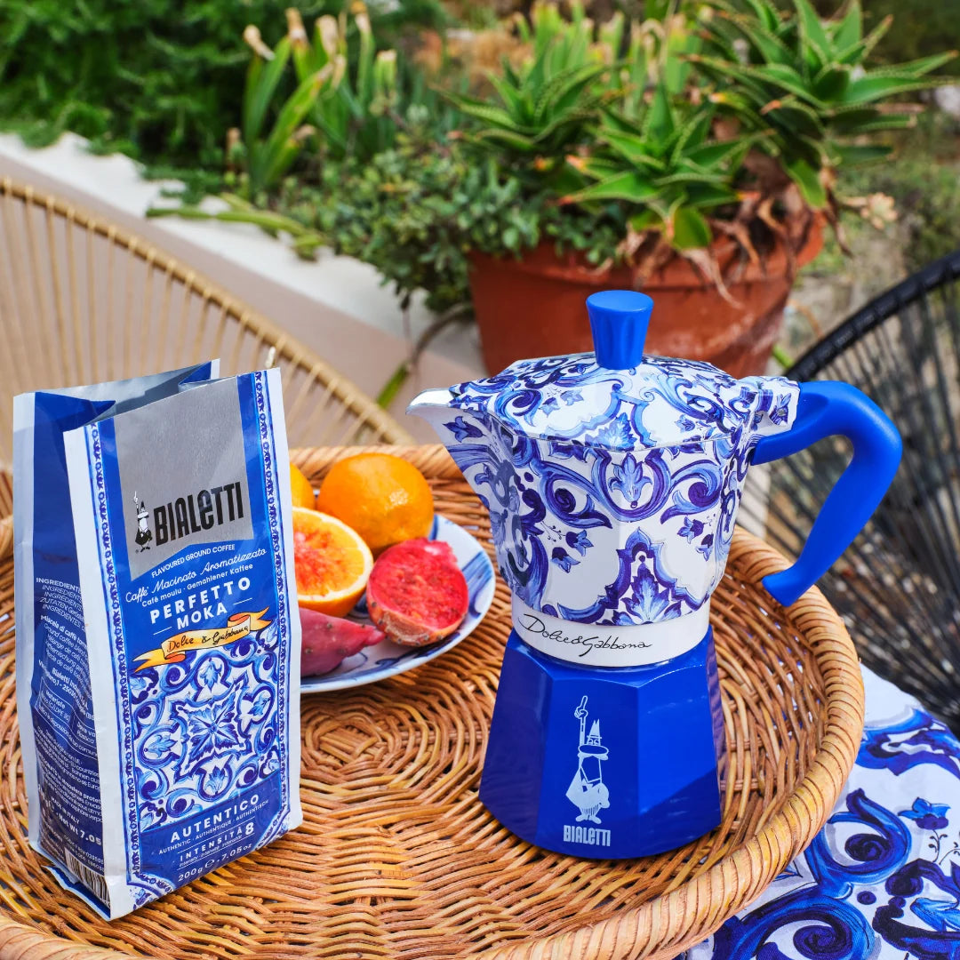 Bialetti Moka Express coffee maker in blue floral design with brewing coffee and fruits on a table