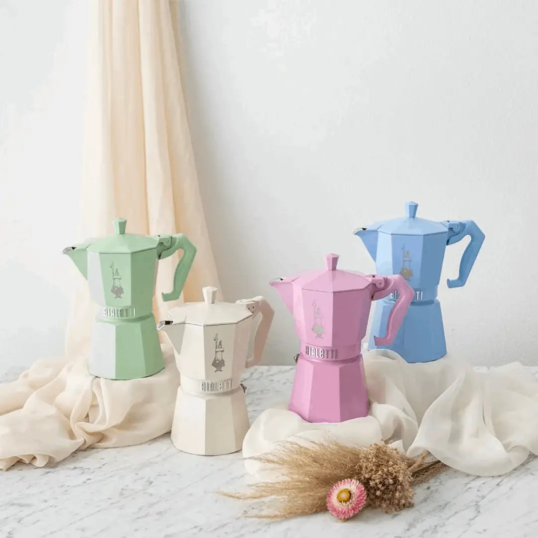 Colourful Bialetti Moka Express coffee makers in pastel green, pink, and blue on a light background