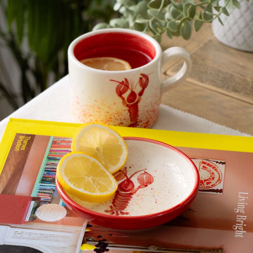 Selbrae House Ceramic Mug with Lobster Design and Butter Dish with Lemon Slices on a Magazine