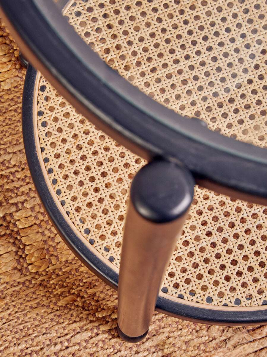 Orsina Console Table with a modern design featuring a glass top and woven rattan shelf