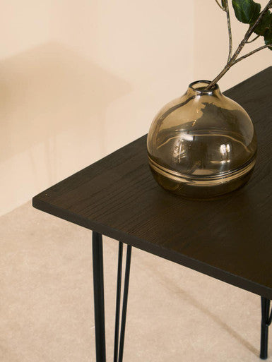 Stylish Orsina Dining Table with a sleek black surface and elegant legs, featuring a decorative glass vase