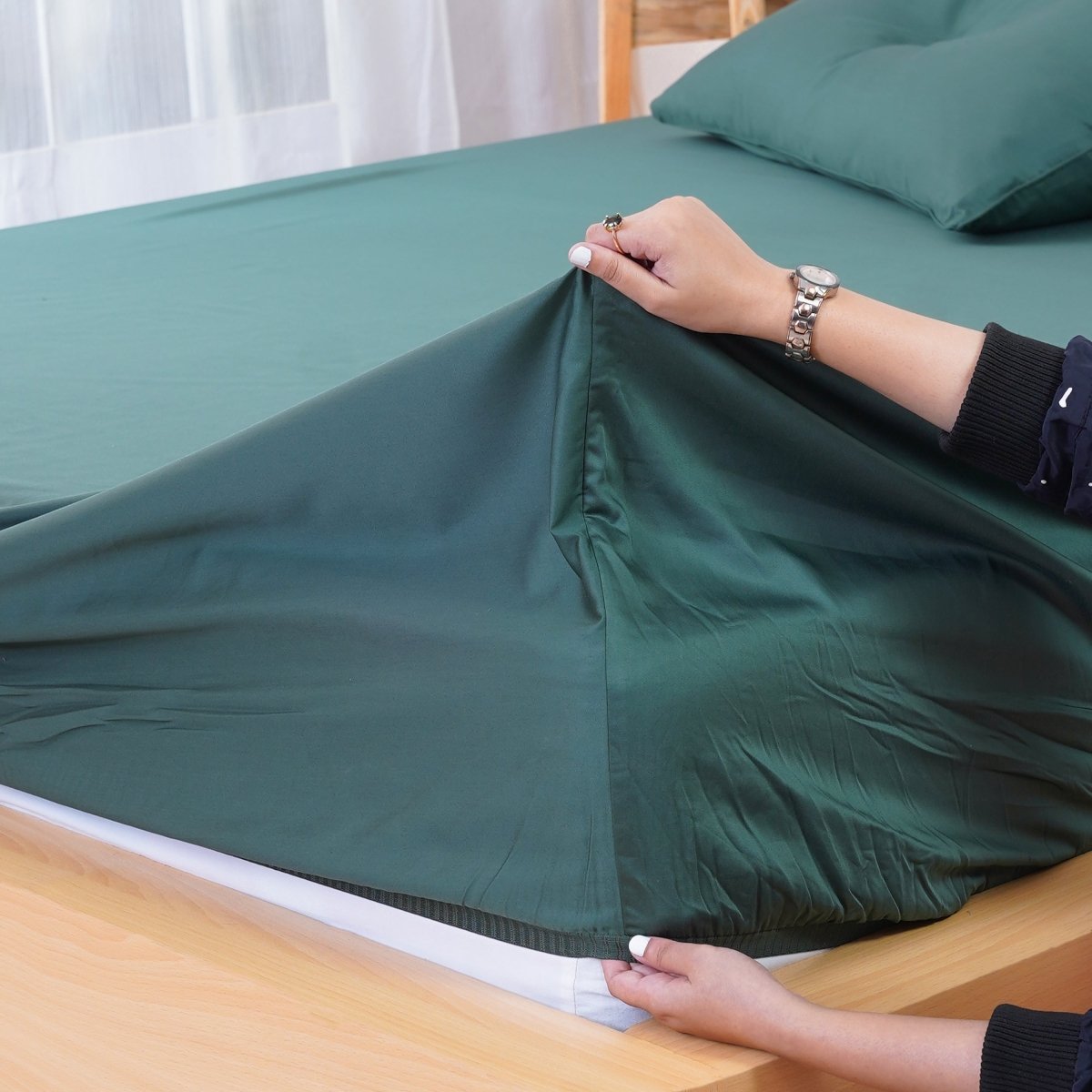 Green fitted sheet by SHEET STORY being adjusted on a mattress for a perfect fit