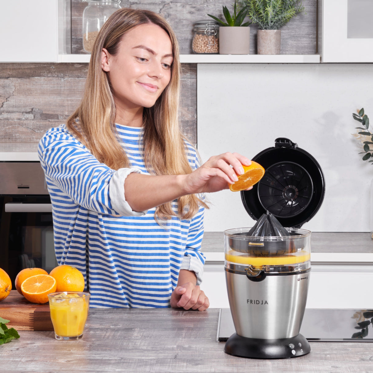 Fridja Citrus Juicer with a woman juicing an orange, ideal for fresh juice enthusiasts
