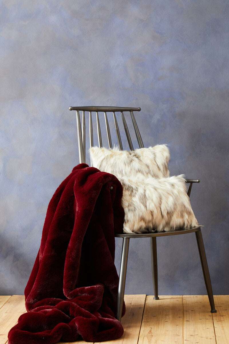 Orsina Fur Cushion in Soft Textures on a Chair with a Red Blanket and Grey Background
