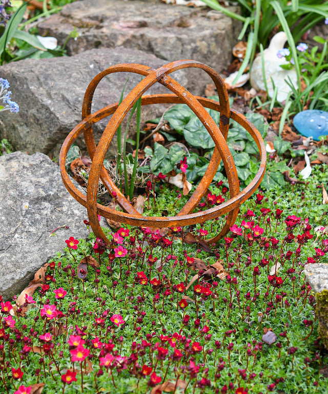 Rustic metal Garden Sphere Ornaments enhancing a garden with vibrant flowers and rocks