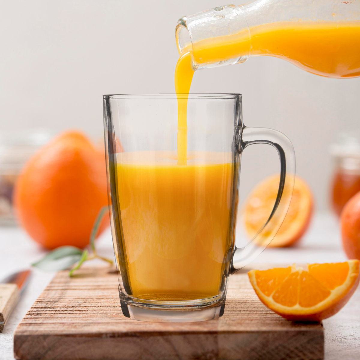 Orsina Glass Mugs poured with fresh orange juice on a wooden board with oranges