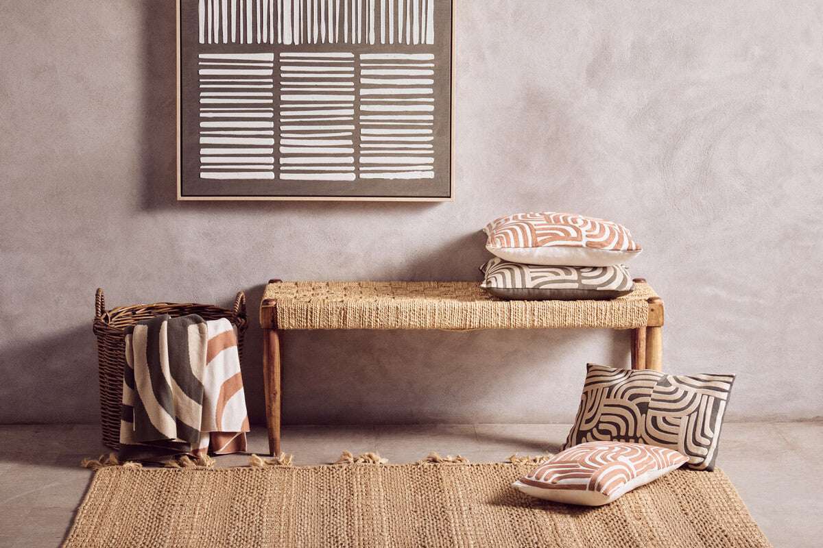 Orsina Green Throw draped stylishly on a woven bench beside patterned cushions and a textured rug