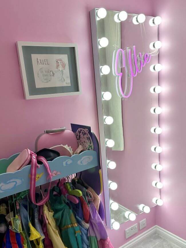 Elegant Hollywood Mirror with bright bulbs, reflecting a stylish pink room and clothes rack