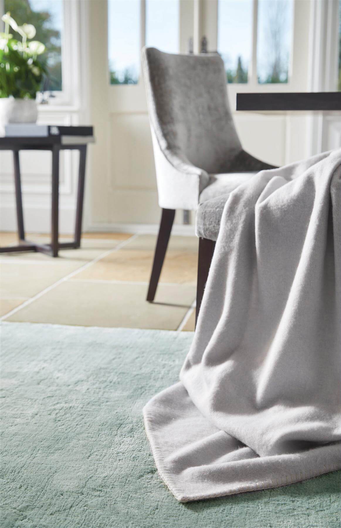Luxurious grey Luxury Rug placed under a dining chair in a bright interior setting