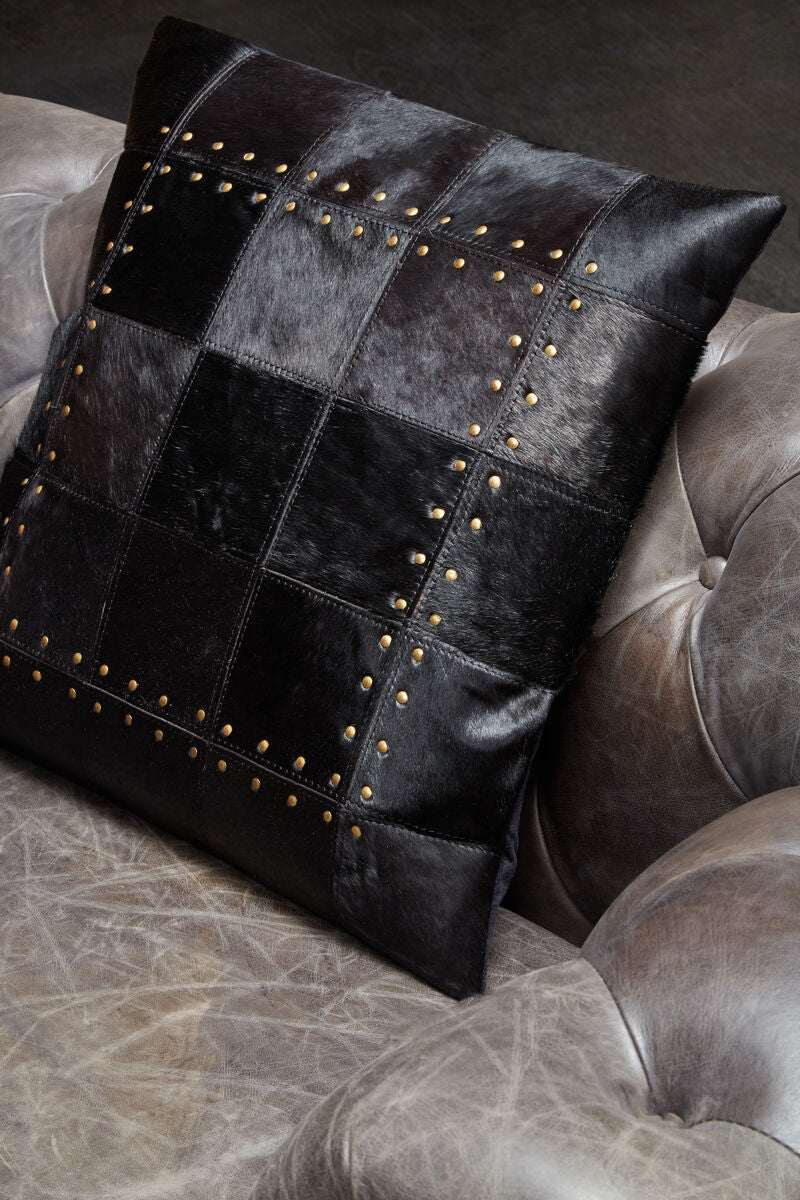 Orsina Patchwork Cushion in black leather with decorative studs on a vintage leather sofa