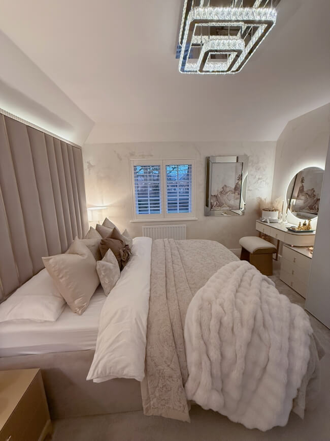 Elegant round mirror above a stylish vanity in a modern, plush bedroom setting with soft bedding and decor
