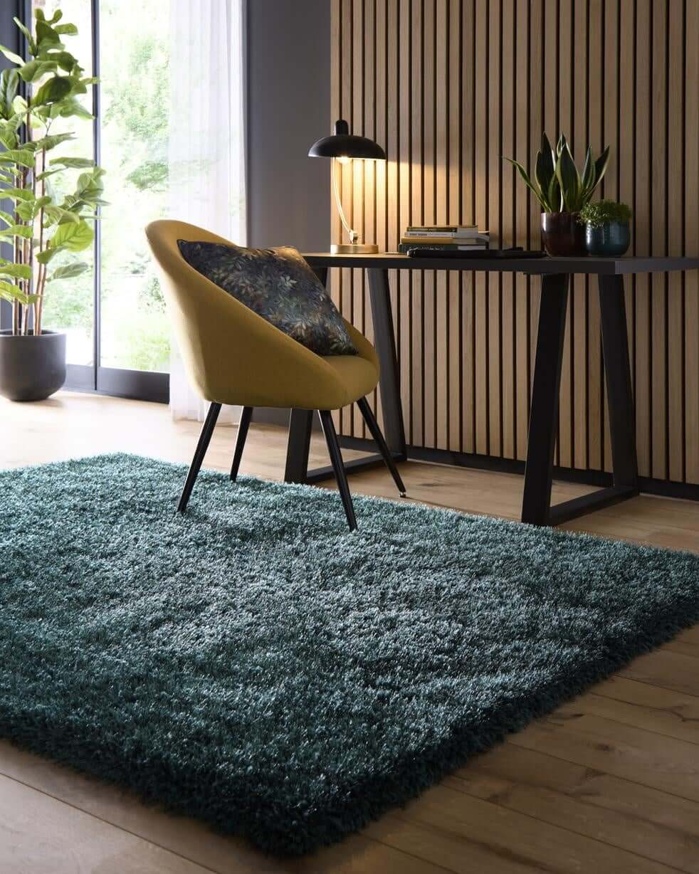 Stylish shaggy rug in teal colour placed under a modern chair and desk in a bright room