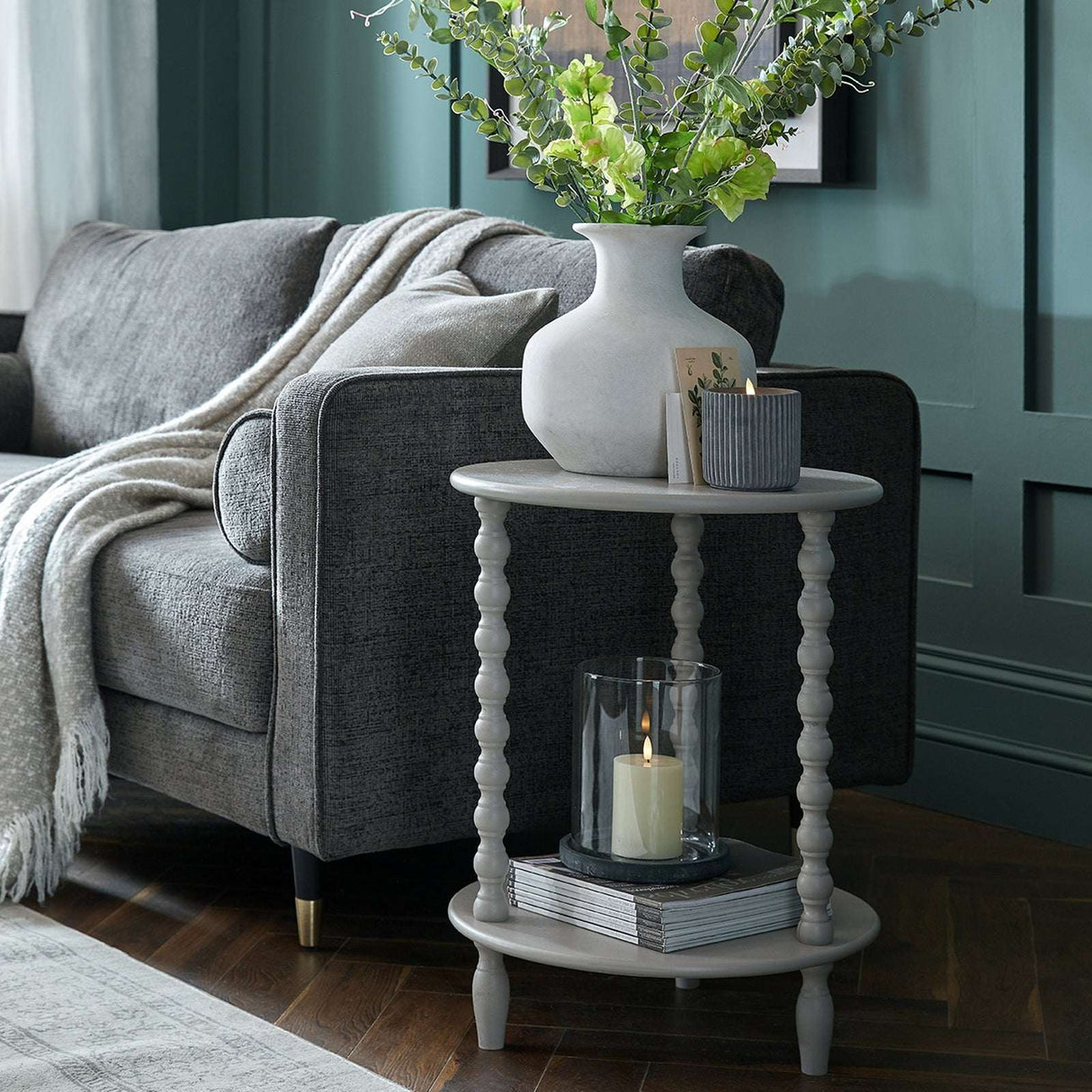 Shades 4 Seasons Side Table with a tiered design, displayed beside a grey sofa and decorated with a vase and candle