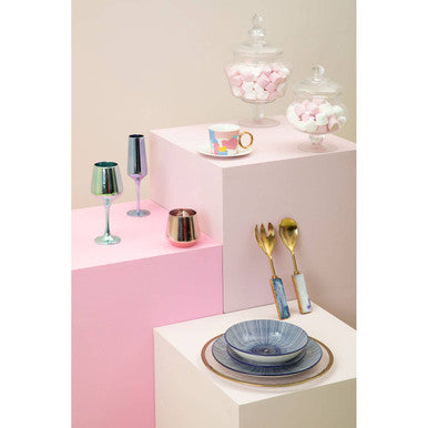 Orsina Serving Set with elegant gold utensils displayed on pastel blocks alongside decorative glassware