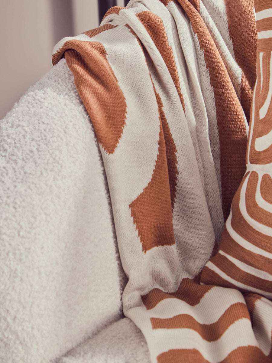 Orsina Terracotta Throw draped over a soft white armchair, featuring a stylish design