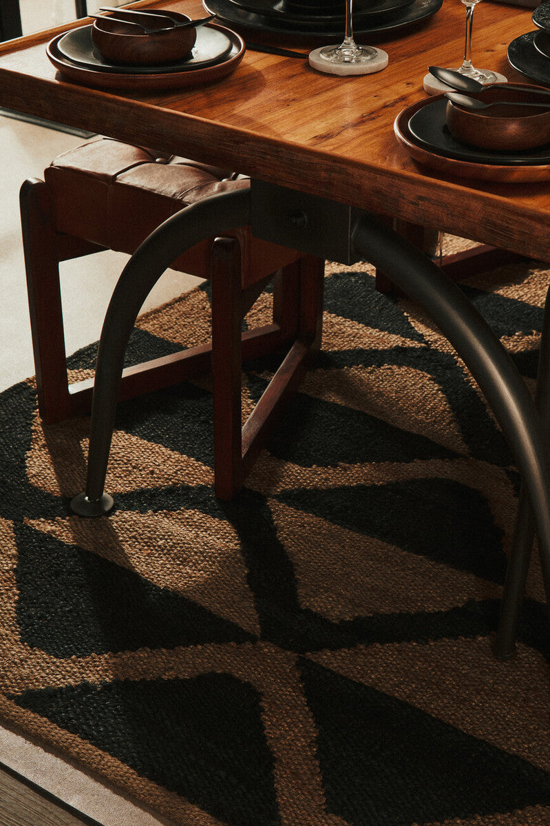 Orsina Hemp Rug with a geometric pattern under a wooden dining table and dark tableware