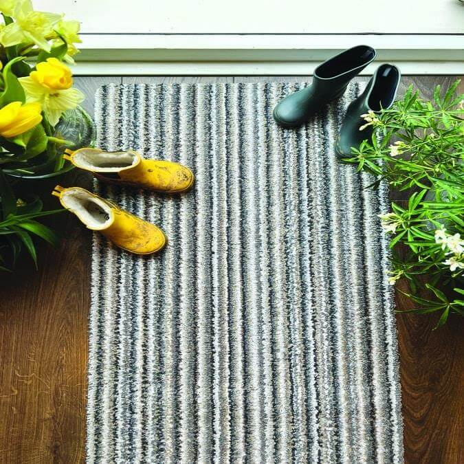 Striped washable mat placed near a door with flower pots and shoes on it