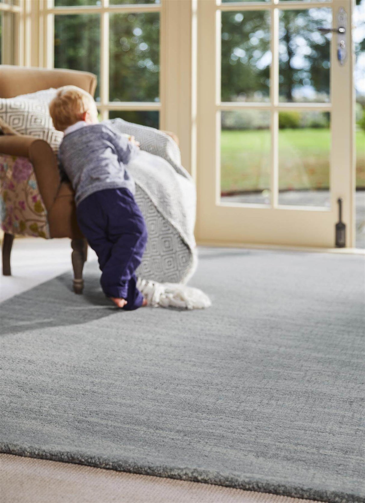 Child playing on a soft grey Wool Rug in a bright living room with large windows