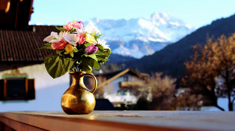 Vibrant arrangement of house plants in a golden vase against a scenic mountain backdrop