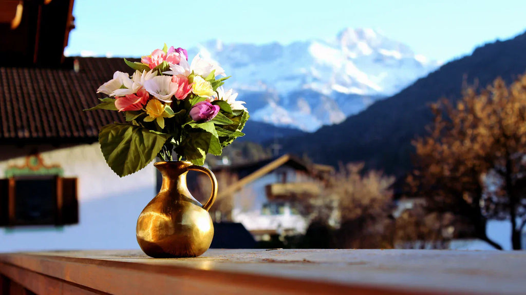 Decorative house plants with colorful flowers in a golden vase on a wooden table with mountain background