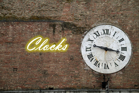 Orsina Wall Clock on a brick wall with a neon sign reading Clocks in the background