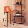 Orsina Bar Chair with a stylish orange seat and a sleek black metal frame beside a modern shelf