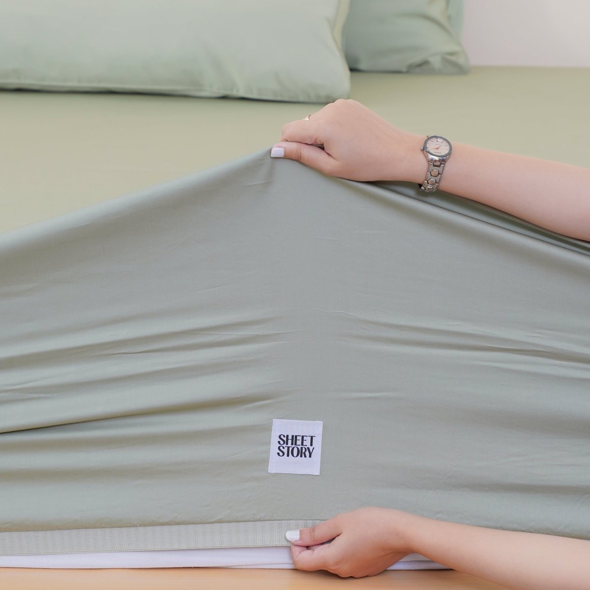SHEET STORY Bedding Set being adjusted on a bed with soft green sheets and matching pillowcases