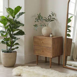 Fishe and Lilly Bedside Table in natural wood finish with two drawers and a pot plant beside it