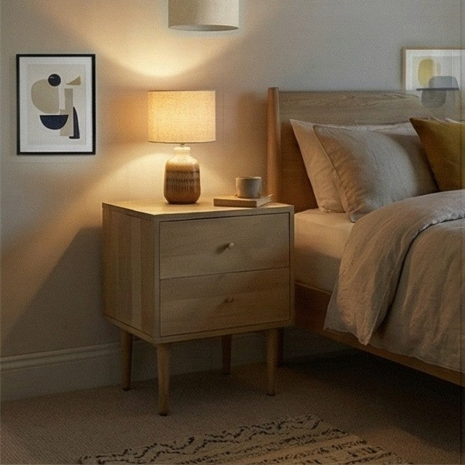 Fishe and Lilly wooden bedside table with two drawers, lamp, and framed art beside a cozy bed