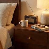 Fishe and Lilly Bedside Table with drawer, lamp, radio, and books beside a bed