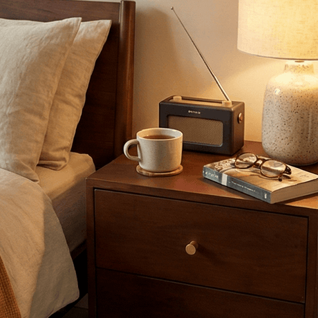 Fishe and Lilly Bedside Table with drawer, lamp, radio, and books beside a bed