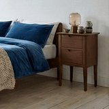 Fishe and Lilly Bedside Table in wood with two drawers beside a stylish bed and blue bedding
