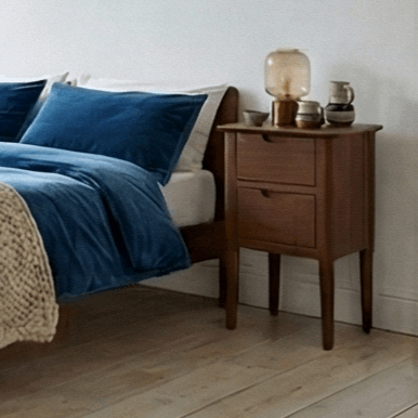 Fishe and Lilly Bedside Table in wood with two drawers beside a stylish bed and blue bedding
