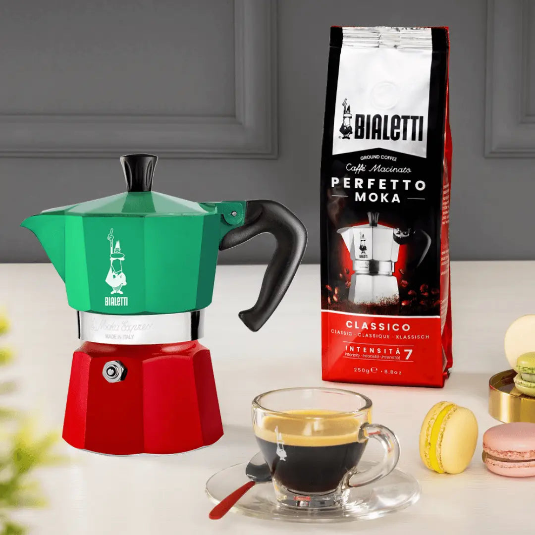 Bialetti Coffee Maker in green and red with a cup of espresso and coffee pack on the side
