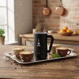 Bialetti Milk Frother in black on a tray with cups of coffee and latte art in a stylish kitchen setting
