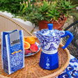 Bialetti Moka Express coffee maker in blue floral design with brewing coffee and fruits on a table