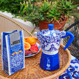 Bialetti Moka Express coffee maker in blue floral design with brewing coffee and fruits on a table