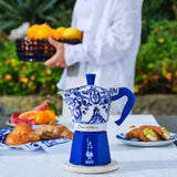 Bialetti Moka Express coffee maker in blue and white design, set on a table with breakfast items