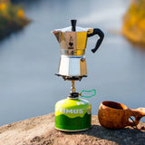 Bialetti Moka Express stovetop coffee maker on a camping stove by a river, perfect for outdoor brewing