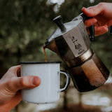 Bialetti Moka Express coffee maker pouring fresh coffee into a white cup outdoors