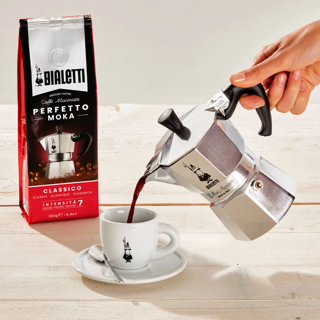 Bialetti Moka Express coffee maker pouring rich coffee into a cup with packaging in the background