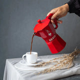 Bialetti Moka Express Coffee Pot pouring fresh coffee into a white cup on a grey surface