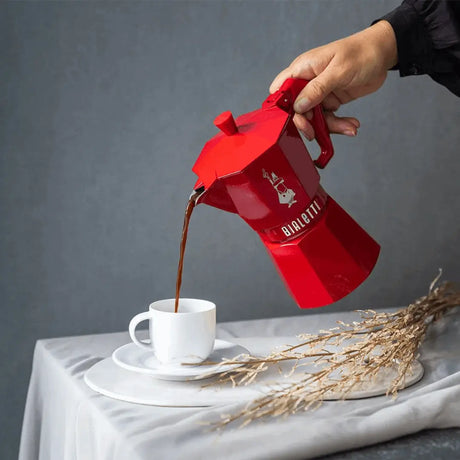 Bialetti Moka Express Coffee Pot pouring fresh coffee into a white cup on a grey surface