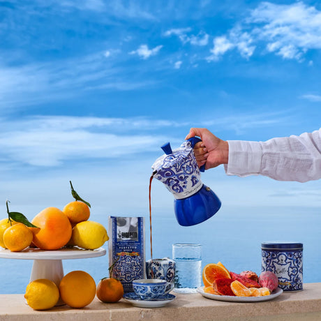 Bialetti Moka Induction coffee maker pouring coffee with citrus fruits on a table by the sea