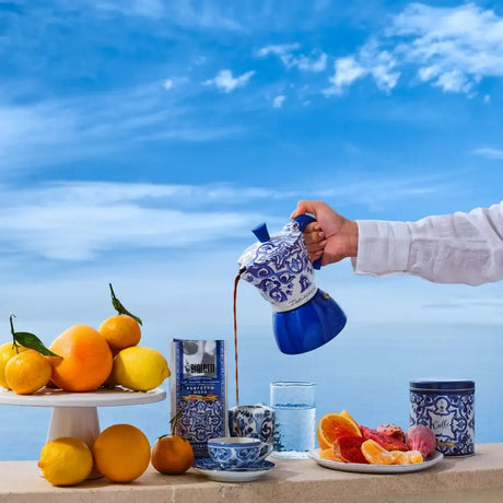 Bialetti Moka Induction coffee maker pouring coffee with citrus fruits on a table by the sea