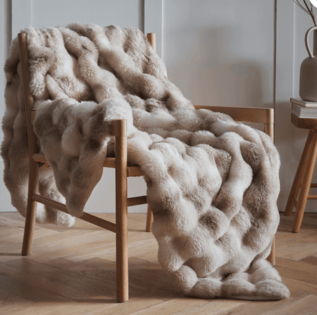 Luxurious soft throw in beige tones draped over a wooden chair for a cosy home atmosphere