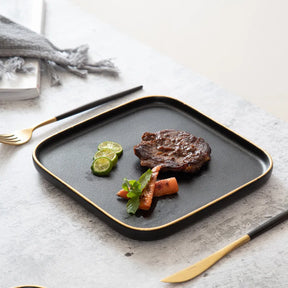 Nisu Home Blino Plates in Black with Gold Trim, featuring a steak and vegetables for elegant dining