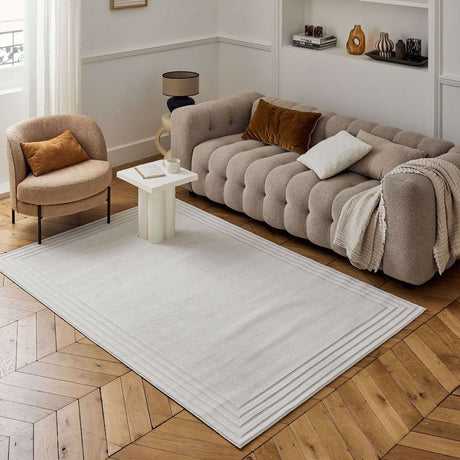 Neutral Bordered Rug displayed in a modern living room with a stylish sofa and elegant decor
