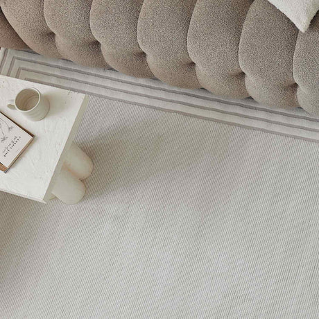 Light-coloured Bordered Rug placed under a plush sofa, enhancing modern home decor