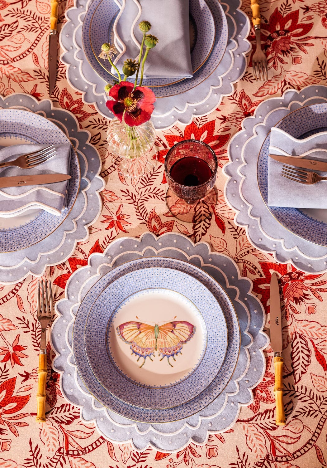 Casa by Josephine Jenno tablecloth featuring a vibrant red floral design with matching plates and cutlery